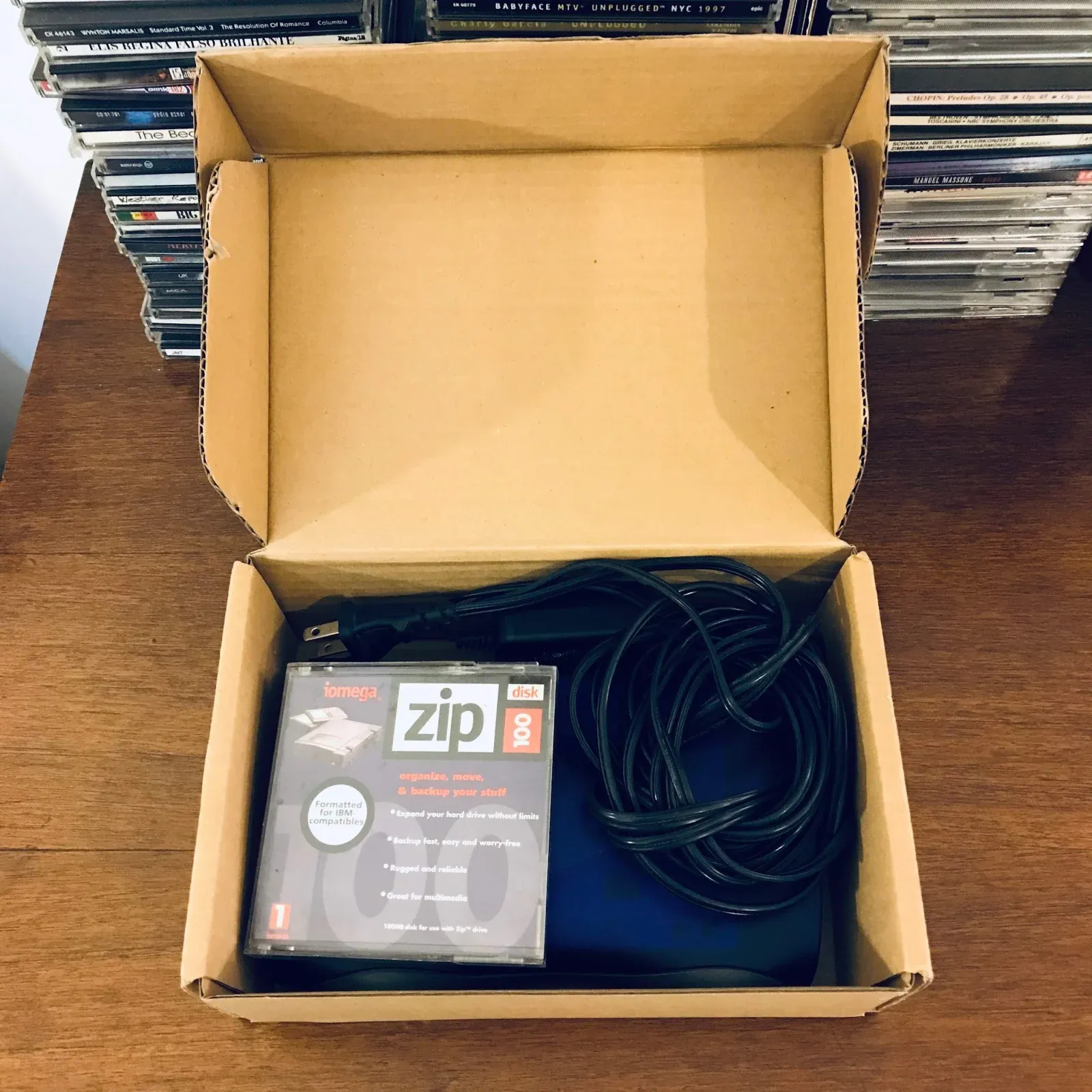 The same Iomega Zip drive packed in an open cardboard box with its disk and power cord.